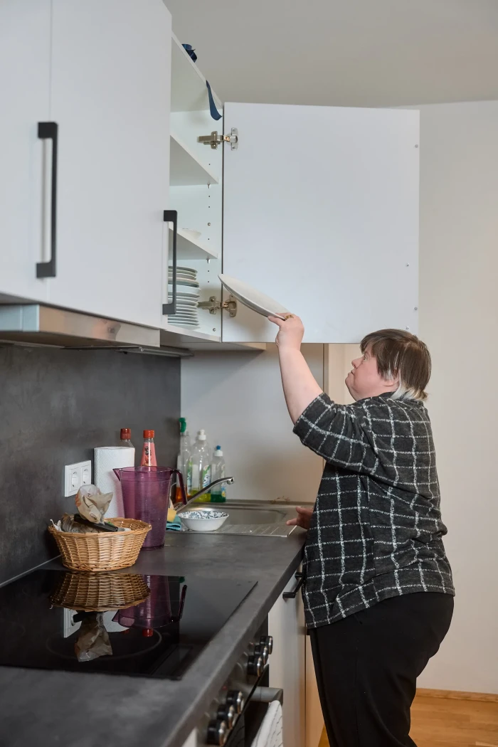 Eine Frau räumt Geschirr in einen Hängeschrank in der Küche.