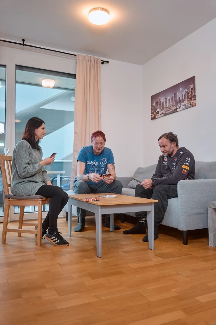 Zwei Männer und eine Frau sitzen an einem Wohnzimmertisch und spielen UNO.