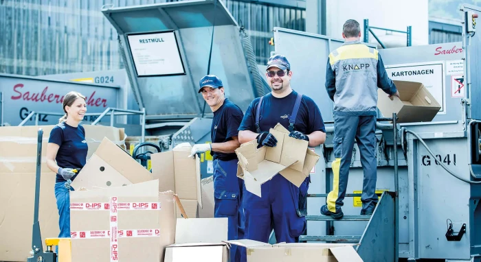 Drei Männer und eine Frau zerlegen Kartons in Overalls von Knapp vor einem Container.